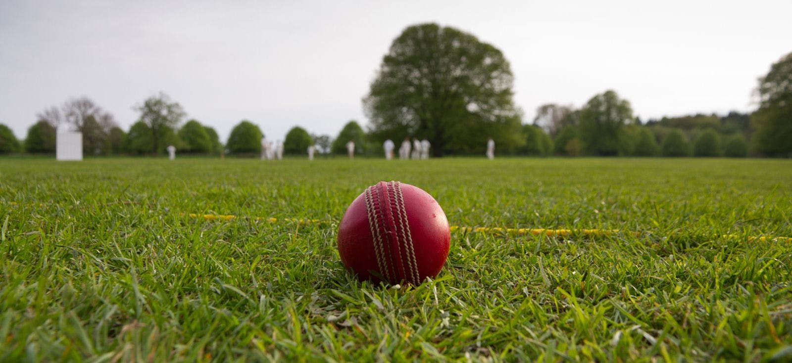 Close up of a cricket ball on a pitch with players in the background