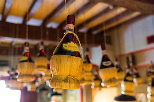 A bottle of red Chianti wine in a wicker basket hanging from the ceiling of a farmhouse