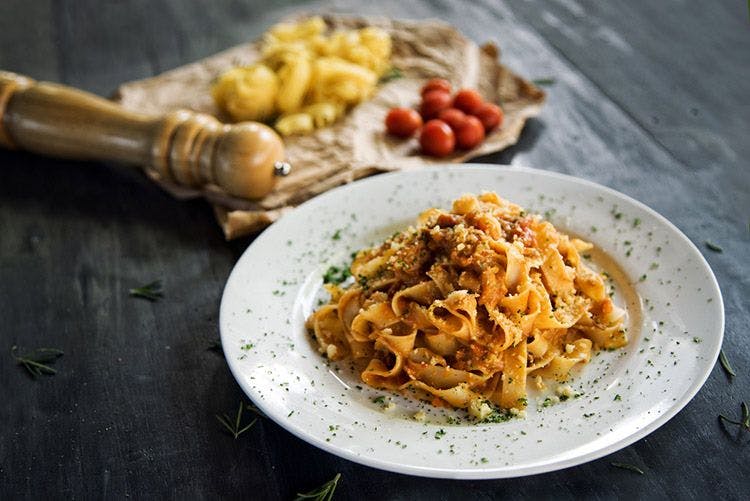 A plate of homemade pasta with a tomato-based sauce and a pepper mill on a black wooden table
