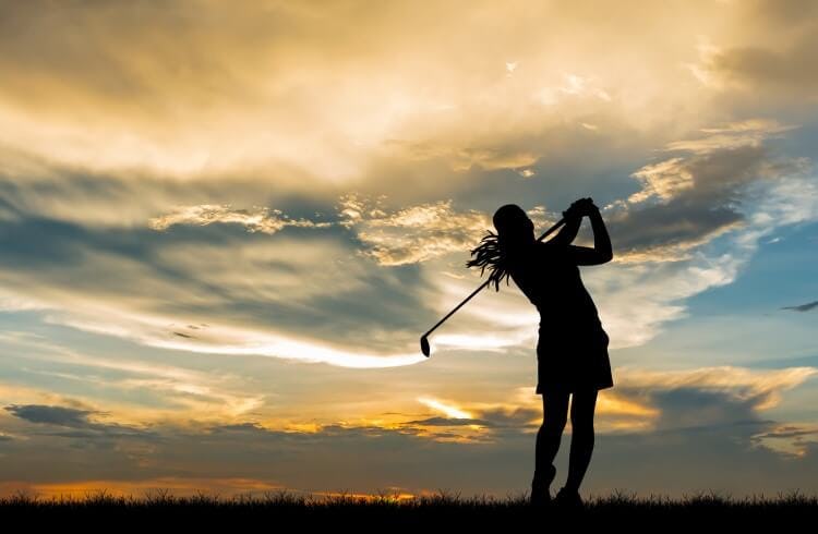 A woman playing golf at sunset