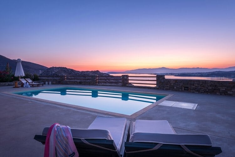 loungers and pool in patio overlooking sea and islands at sunset