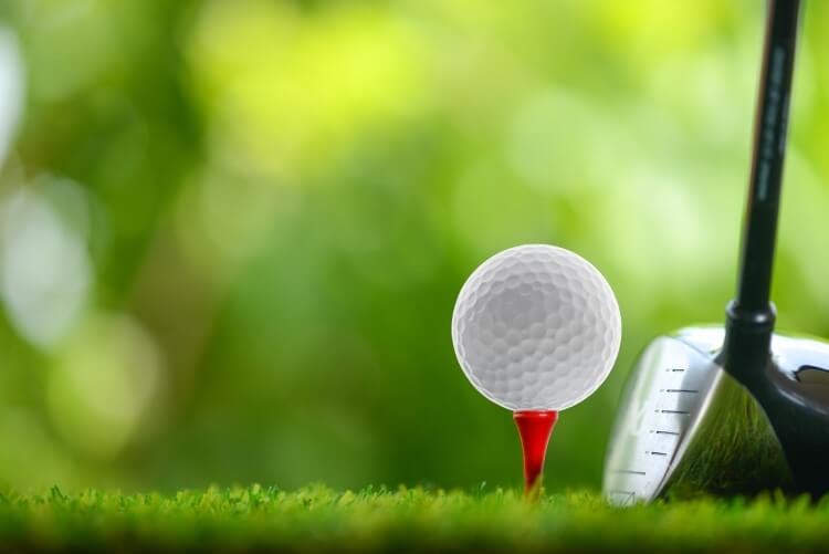 A macro shot of a golf ball on a tee and a golf club head