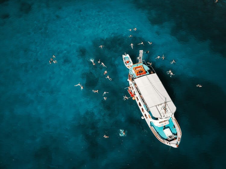 An ariel shot of a white pleasure boat with people swimming in clear blue water around it