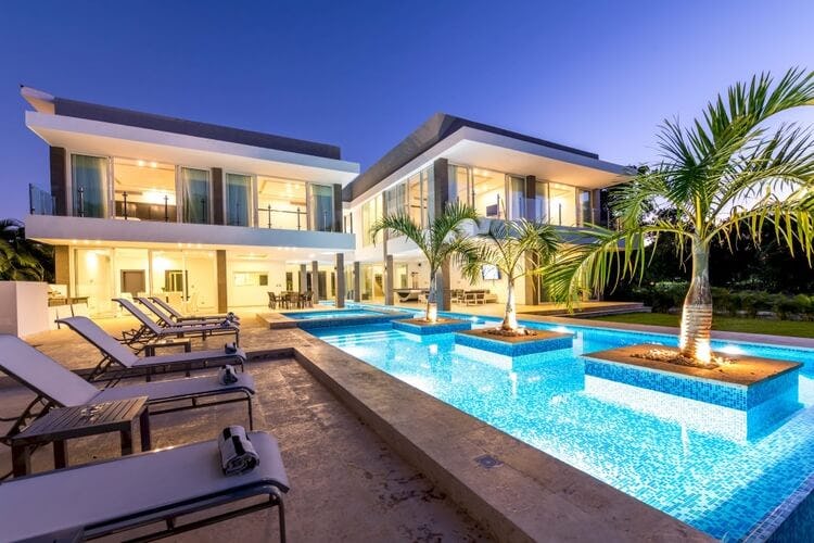modern villa at dusk with pool and platform in center with palm trees