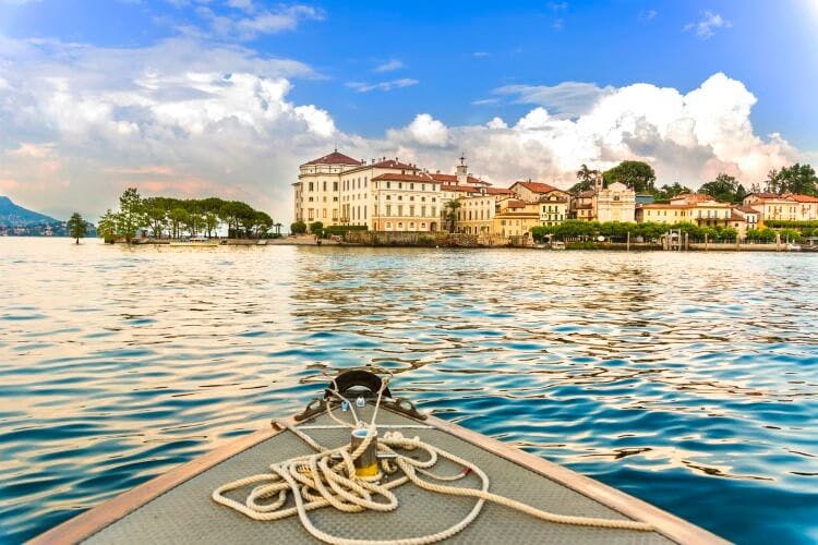 A view from the bow of a small rowing boat on the water of Lake Maggiore showing a small town on the shores of the lake