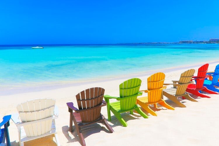 Colorful wooden beach chairs in a straight line along a white sand beach in the Caribbean