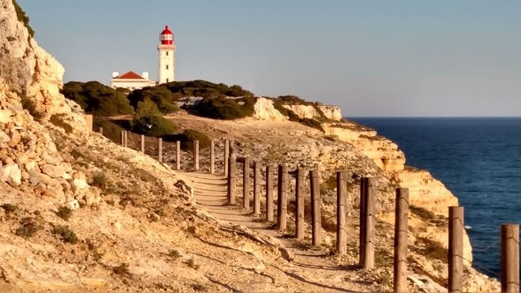 A clifftop pathway leading to a lighthouse on the Percurso dos Sete Vales Suspensos