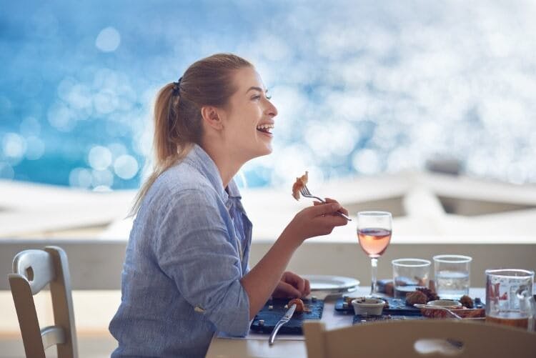 woman smiling and eating next to ocean