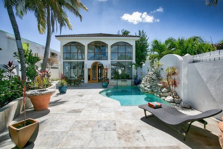 Vittoria vacation rental in Saint Martin - a large home with arched windows, a private pool and spacious tiled patio area with sun lounger and potted tropical trees
