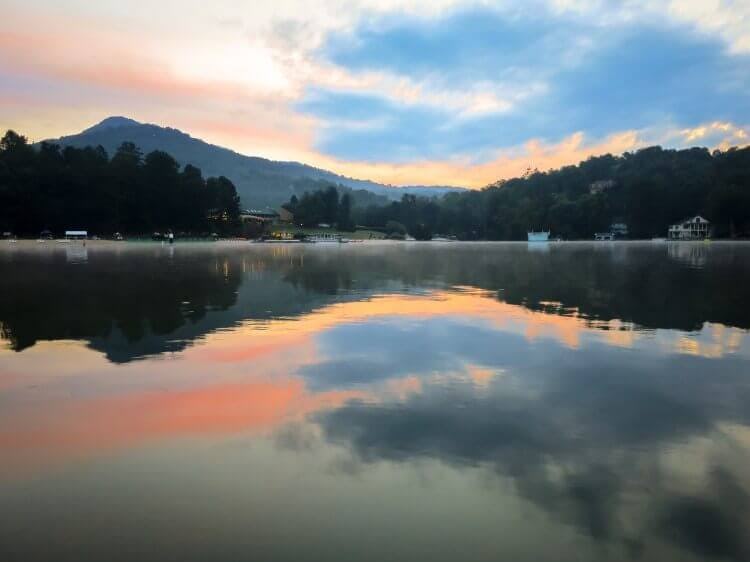 Sunrise over Lake Lure with trees and mountains reflected in the still water