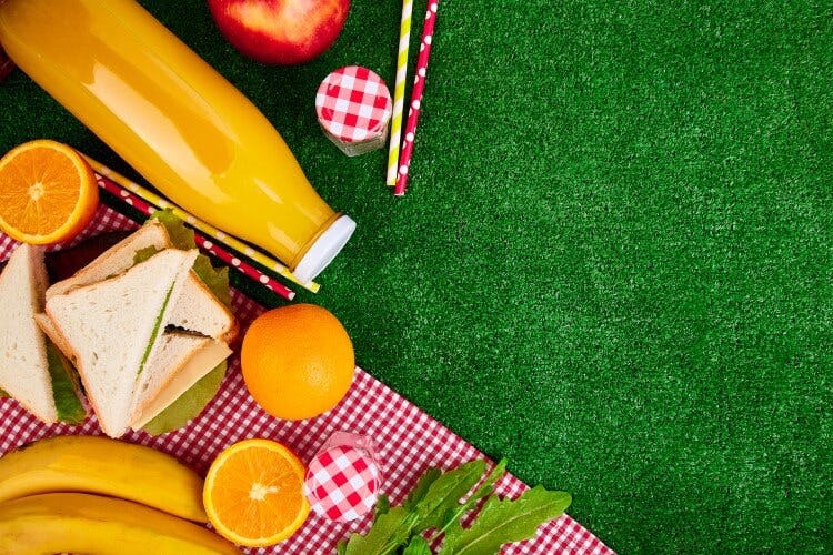A picnic blanket with juice, fruit, sandwiches and jam