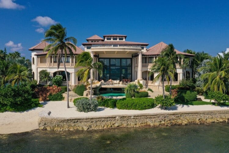 Kempa Caribe vacation rental in the Cayman Islands, a grand beachfront mansion with large panoramic glass windows and landscaped shrubbery at the front