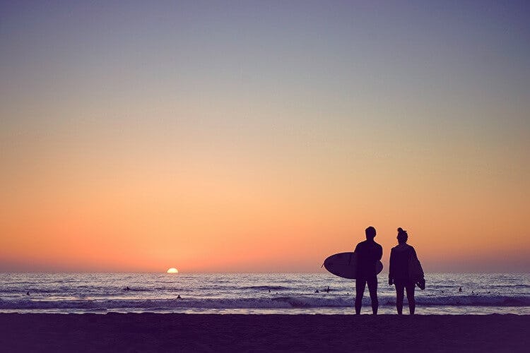 couple on beach at sunset with surf board