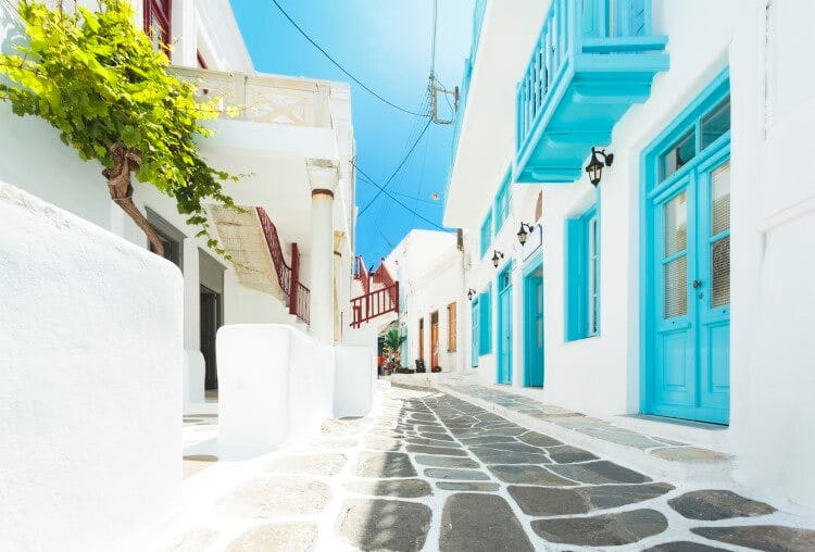 A cobbled street in Chora, Mykonos, with white-painted buildings with blue windows and doors