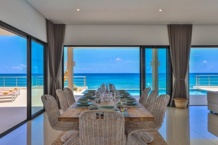 Alma vacation rental dining room with a table and chairs looking out of a panoramic window with a view of the Caribbean Sea