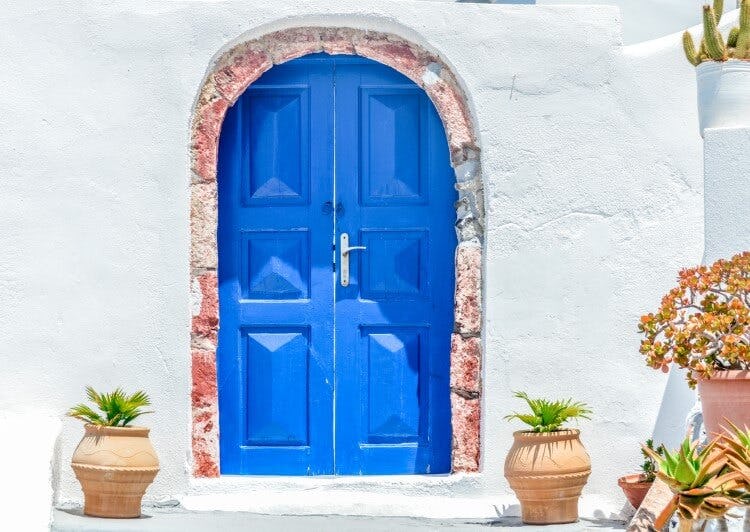 An arched door that is painted blue against a white wall of a building in Mykonos