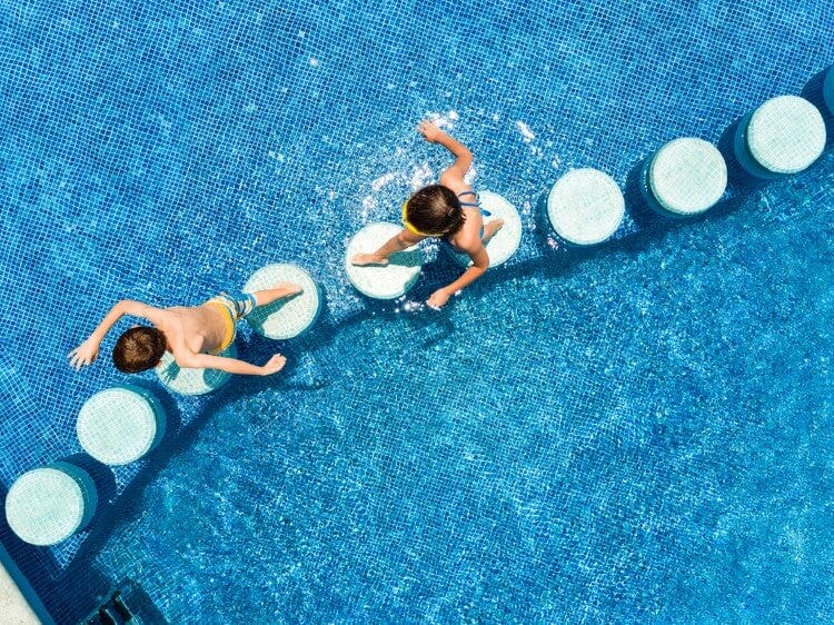 Two children running across stepping stones in a swimming pool