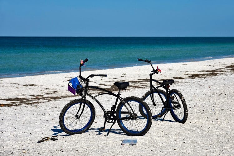 Two bikes standing in white sand on a beach by the ocean
