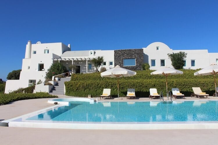 large white villa with patio and pool with loungers