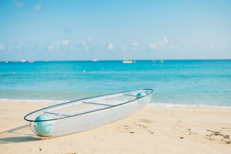 A clear canoe resting on the white sand of a Turks and Caicos beach. There are small white boats on the horizon