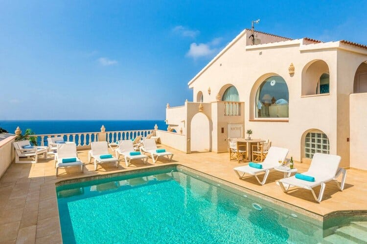 tan villa with pool and loungers overlooking ocean