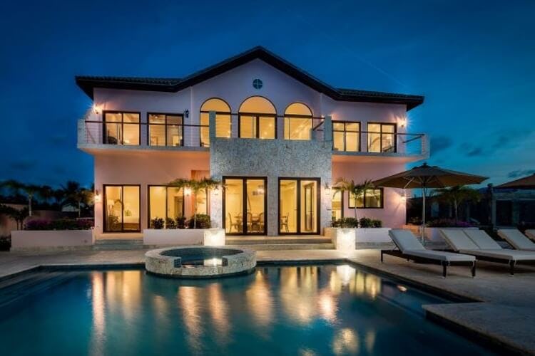 mansion style villa lit up at dusk with jacuzzi, pool and loungers