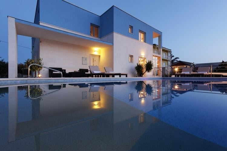 white and blue villa at dusk with pool in foreground