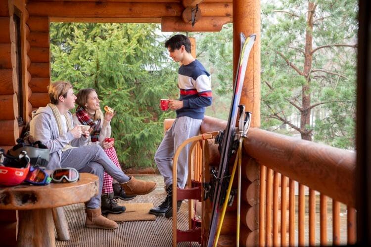 3 people on a cabin balcony with skis propped against the railing
