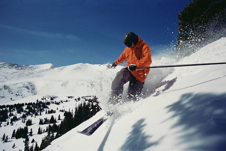 A man in a bright ornage jacket skiing down a steep hill covered in powder snow in Breckenridge, Colorado
