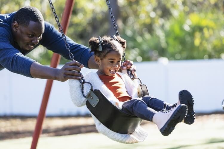 child and father playing with swing