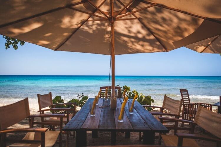 A table and chairs covered by a beach umbrella at a restaurant in the Caribbean
