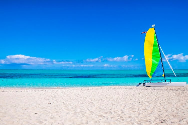 A green and yellow-sailed windsurfer on a white sand beach in Turks and Caicos