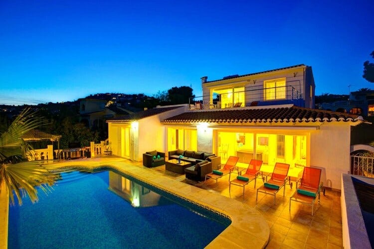 lit up white villa at dusk with pool