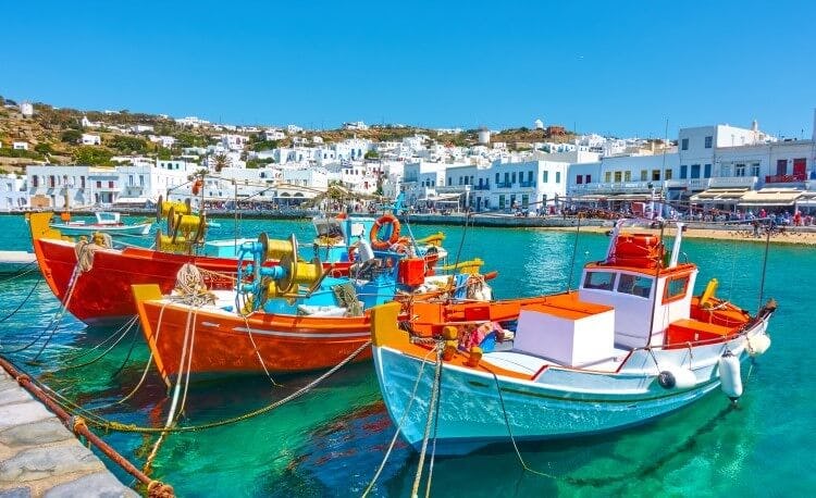 Three fishing boats moored in a harbor with Mykonos Town's white sugar-cube buildings behind
