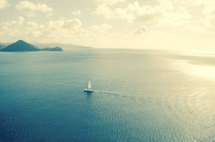 A lone sailboat sailing on a smooth Caribbean Sea with islands in the background