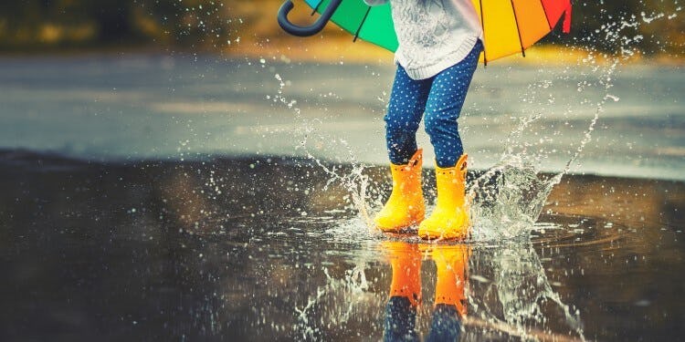 A young child in  yellow wellies splashing in a puddle