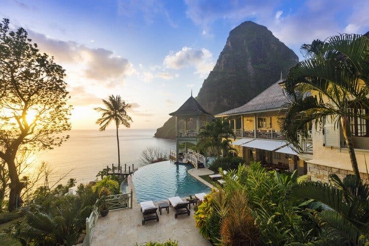 Arc En Ciel vacation rental in Saint Lucia with a view of the Pitons, palm trees, and the sun setting over the Caribbean Sea