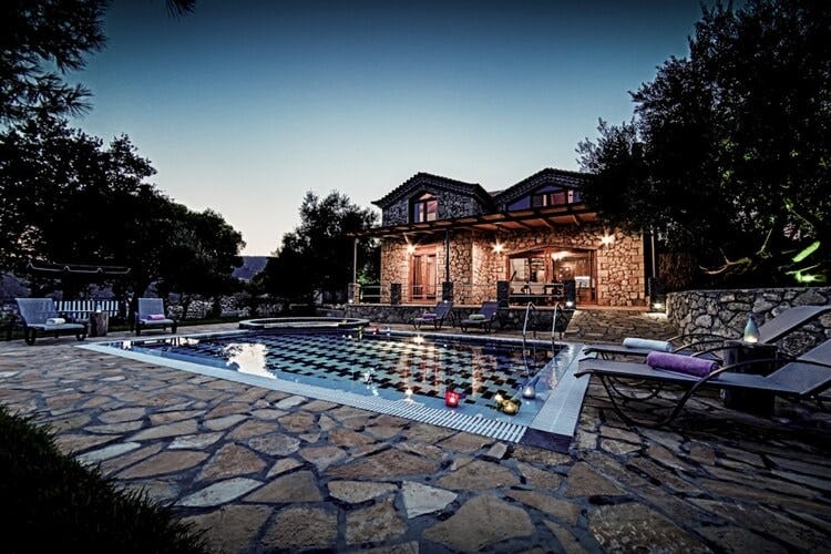 rustic stone villa lit up at dusk with pool
