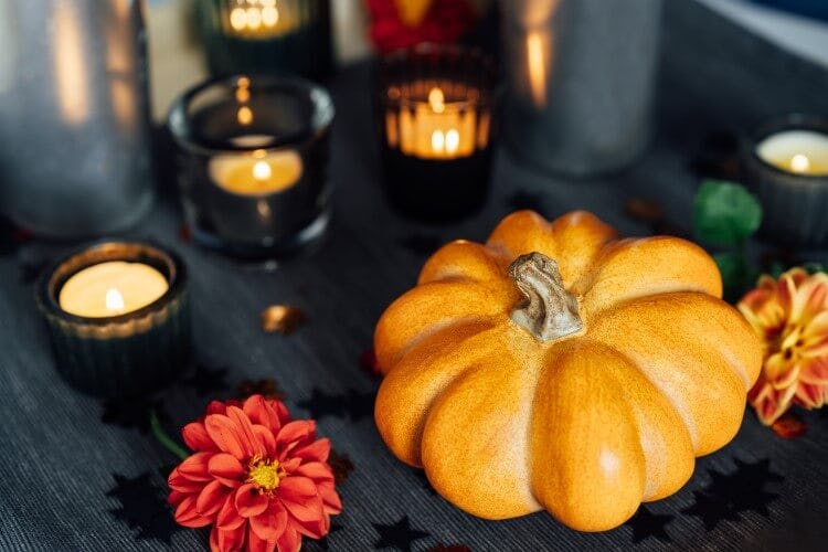 A small orange pumpkin on a black wood table surrounded by orange flowers and candles