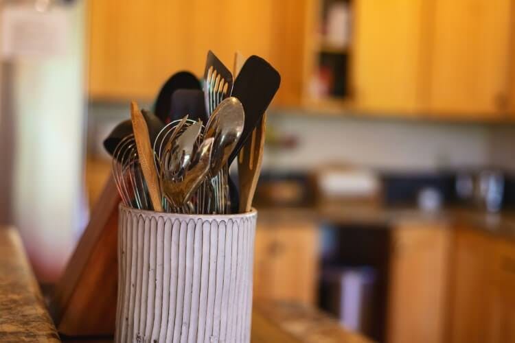 A kitchen with a pot holding various cutlery including forks, knives, and spoons