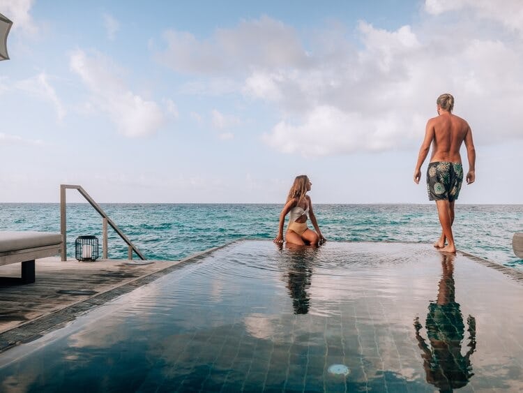 a couple standing and sitting on the edge of an infinity pool
