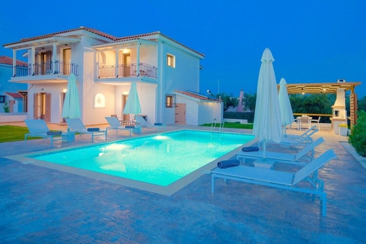 white villa at dusk with pool and loungers