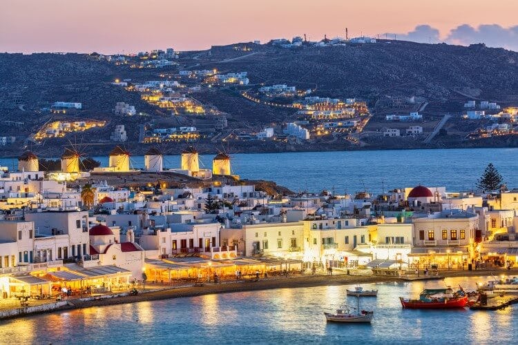 The old town of Mykonos at sunset, with buildings lit up