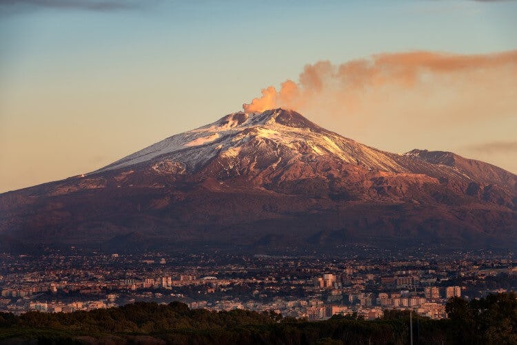 Mount Etna in Sicily, with snow at the peak and a plume of smoke from the crater