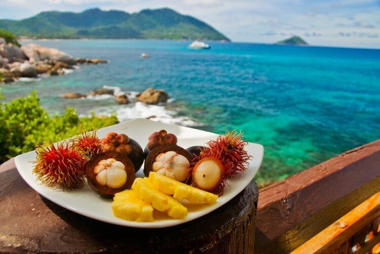 A variety of tropical fruits on a plate balanced on a ledge overlooking the ocean in Phuket