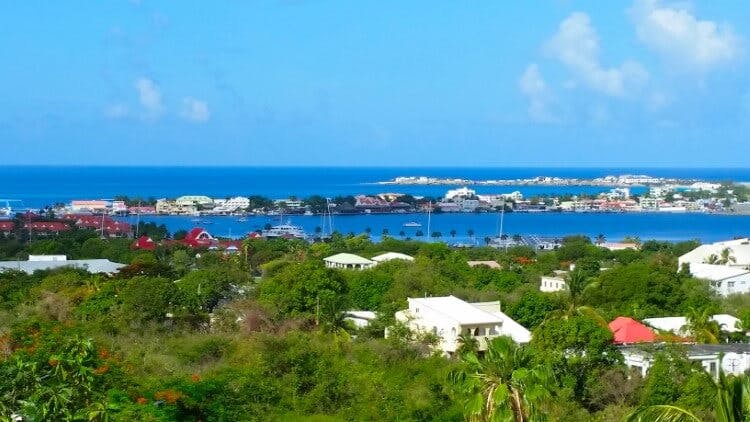 A panoramic image of Simpson bay in Saint Martin, with a view of the sea, sky, boats in the harbor, and buildings scattered through tree covered streets