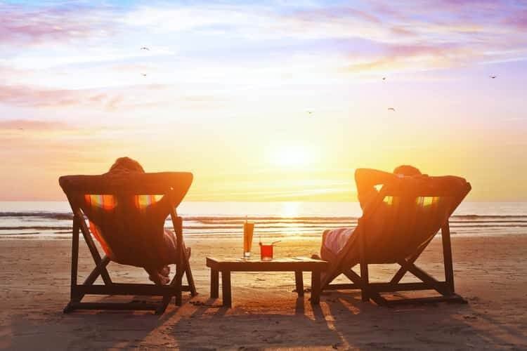 two people relaxing on chairs on beach at sunset