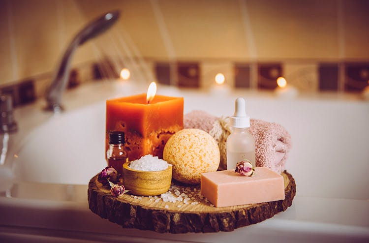 An in-home spa set up with candles, bath salts, loofahs, oils, and more