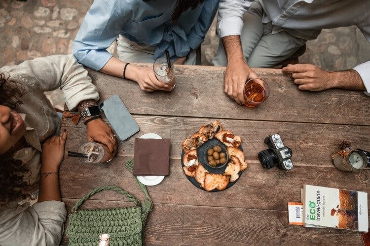 Friends sit around an outdoor table in Italy, enjoying a small plate of bread appetizers and drinks