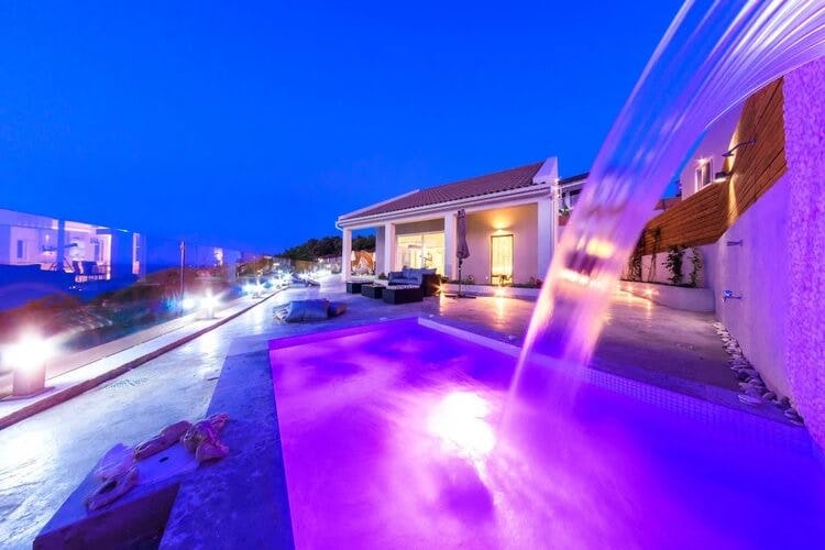 White villa at dusk with pool and fountain lit up purple
